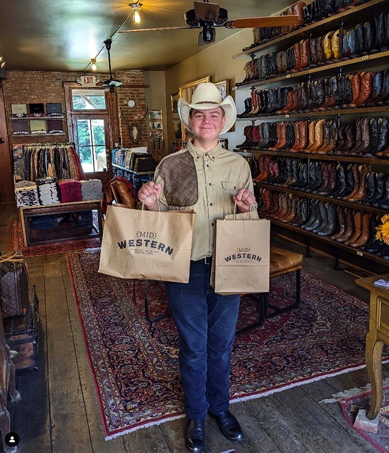 Young customer in western wear holding newly purchased bags at (Mid)Western Second Hand shop in Somerset, Perry County, Ohio.