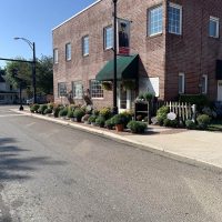 Exterior view of Seals Flowers & Gifts - red brick building with green awning entrance and row of plants on the sidewalk.