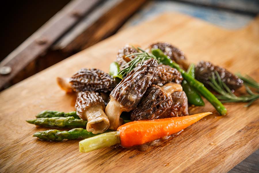 Cooked Morel mushrooms with carrots and asparagus on a cutting board.