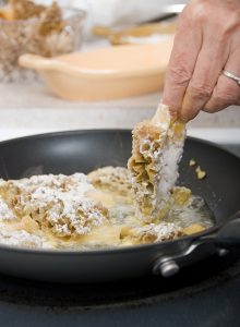 Hand dropping lightly floured Morel mushroom into frying pan with other mushrooms.